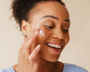Woman applying cream to her face with a neutral background