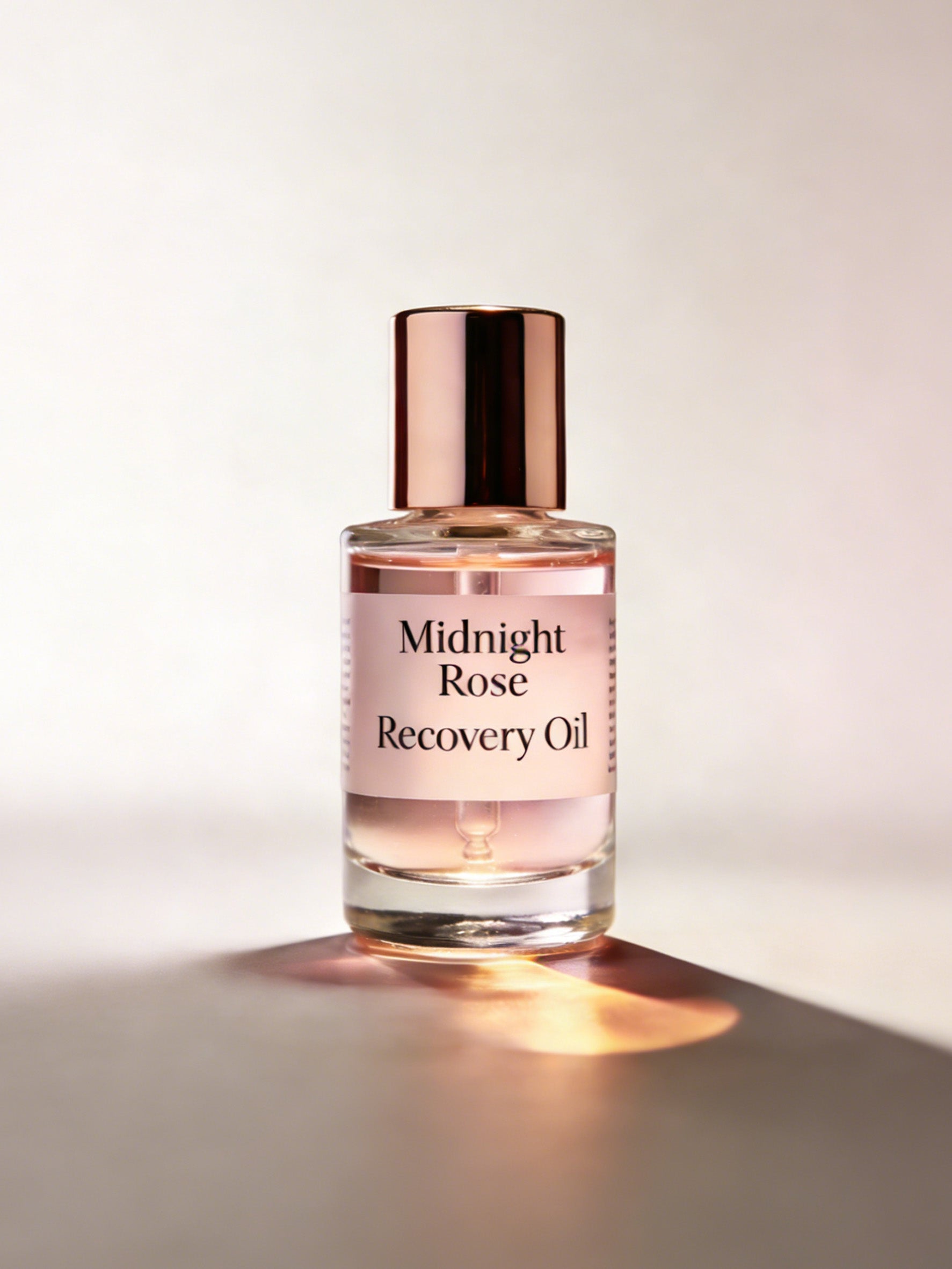 Bottle of Midnight Rose Recovery Oil with a rose gold cap on a light background